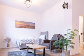 A modern bedroom with a bed, bedside table, lamp, chair, and a painting of a sunset over a beach.