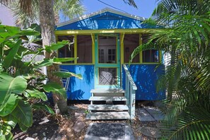 A small, single-story building with a porch, surrounded by tropical vegetation. - BlueDolphin Cottage Walk To Siesta Beach (Siesta Key)