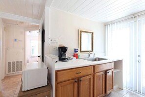 A kitchen with a white refrigerator, a coffee maker, and a sink. There is a wooden cabinet with drawers and a mirror above the sink. - BlueDolphin Cottage Walk To Siesta Beach (Siesta Key)