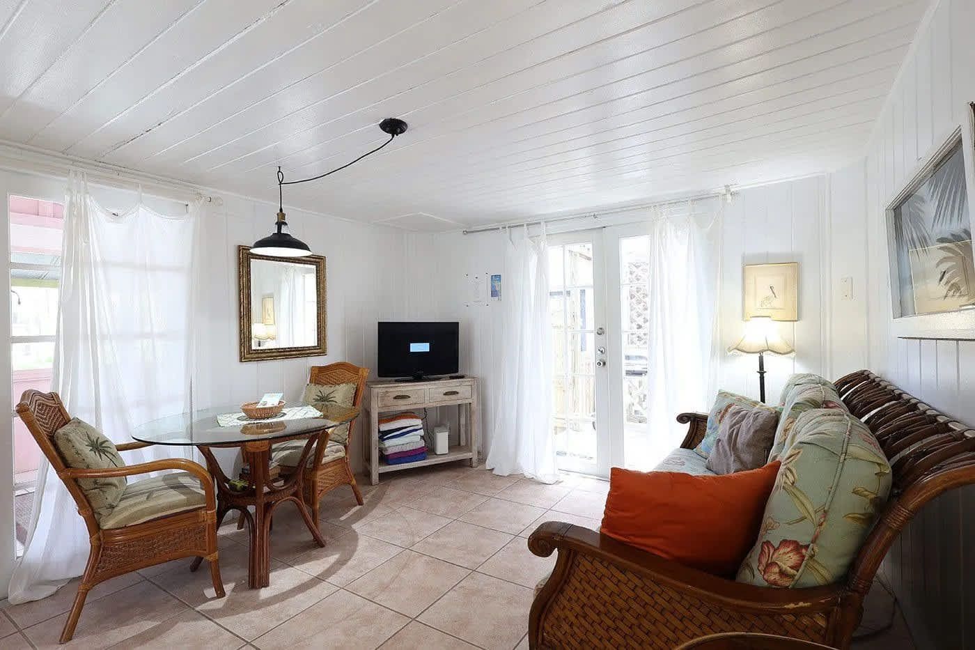 A room with a dining table, chairs, a television, a sofa, and a lamp.