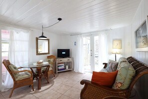 A room with a dining table, chairs, a television, a sofa, and a lamp.