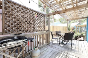A wooden deck with a grill, chairs, and a table.