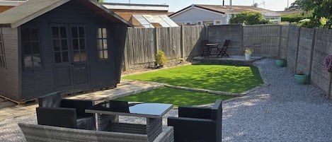 A backyard with a small lawn, a wooden shed, and a seating area with chairs and a table.