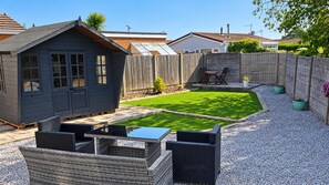 Ein Garten mit einer Terrasse, einem kleinen Schuppen und einem eingezäunten Bereich.