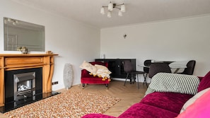Ein Wohnzimmer mit Kamin, einem roten Sofa, einem gemusterten Teppich und einem Essbereich mit Tisch und Stühlen.