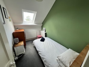 A small, single-bed room with a sloped ceiling, a radiator, a window, and a green wall. - Large home, 6 bedrooms, private parking, gardens (Barnstaple)