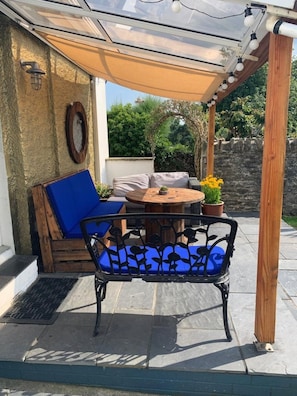 A covered patio area with a table and chairs, a blue cushioned sofa, and a pergola with string lights. - Large home, 6 bedrooms, private parking, gardens (Barnstaple)