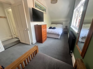 A bedroom with a bed, a dresser, a television mounted on the wall, and a window. - Large home, 6 bedrooms, private parking, gardens (Barnstaple)
