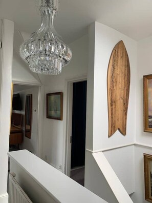 A staircase with a white railing, a chandelier, and a wooden surfboard decoration on the wall. - Large home, 6 bedrooms, private parking, gardens (Barnstaple)