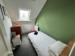 Une chambre avec un lit simple, un radiateur, une fenêtre et un petit tabouret.