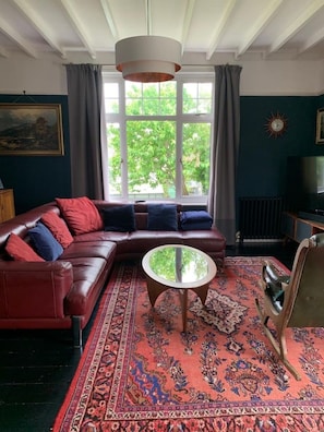 Un salon avec un canapé d’angle, une table basse ronde et une grande fenêtre avec des rideaux.