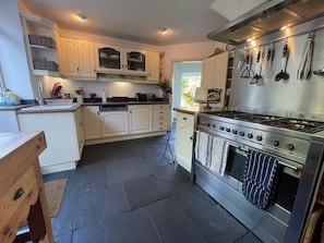 A kitchen with white cabinetry, a stainless steel stove, and a tiled floor. - Large home, 6 bedrooms, private parking, gardens (Barnstaple)