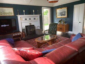 A living room with a red leather sofa, a glass coffee table, a fireplace, a television, and a framed picture on the wall. - Large home, 6 bedrooms, private parking, gardens (Barnstaple)