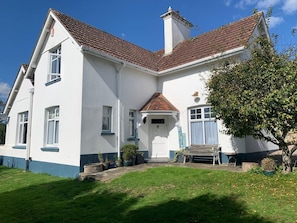 A two-story house with a red-tiled roof, white walls, and a small front porch with a bench. - Large home, 6 bedrooms, private parking, gardens (Barnstaple)
