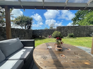 An outdoor patio with a wooden table, cushions, and a flower arrangement. - Large home, 6 bedrooms, private parking, gardens (Barnstaple)