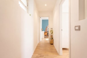 A hallway with wooden flooring, white walls, and a door leading to a room with a blue accent wall. - Ravanas City Escape | Stylish 2BR Apartment (Bari)