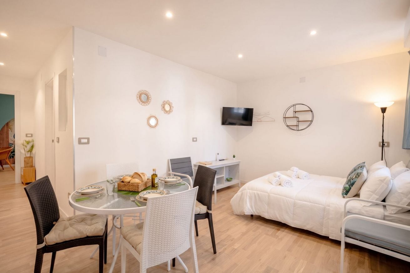 A modern, well-lit room with a dining area, a bed, and a TV mounted on the wall.