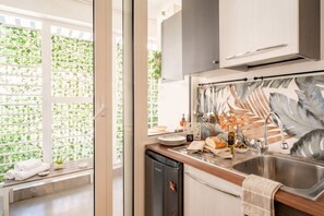 A modern kitchen with a built-in dishwasher, a stainless steel sink, and a window with a view of greenery. - Ravanas City Escape | Stylish 2BR Apartment (Bari)