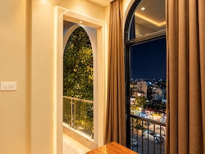 A room with a view of a cityscape at night, a window with curtains, and a door leading to another space. - Hotel Ishaan Palace (Ujjain)