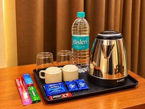 A tray with a Bisleri water bottle, a coffee maker, two mugs, and assorted snacks including Tetley tea bags, sugar packets, and Nescafe. - Hotel Ishaan Palace (Ujjain)