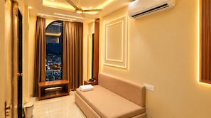 A hotel room with a bed, bedside table, and a view of a cityscape through a window. - Hotel Ishaan Palace (Ujjain)