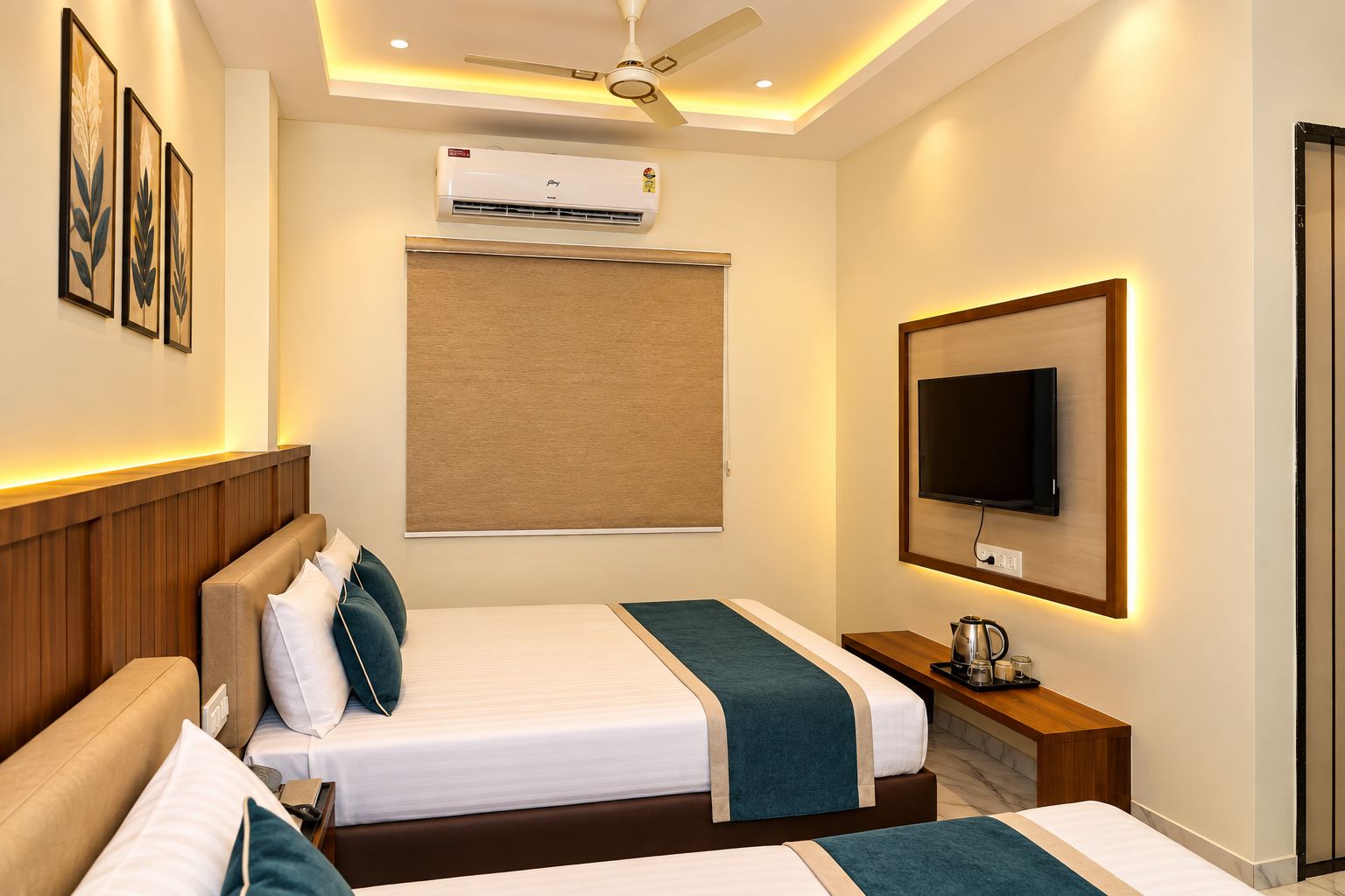 Une chambre d’hôtel avec deux lits, un ventilateur de plafond, un appareil de climatisation, un téléviseur fixé au mur et une table de chevet avec une bouilloire.