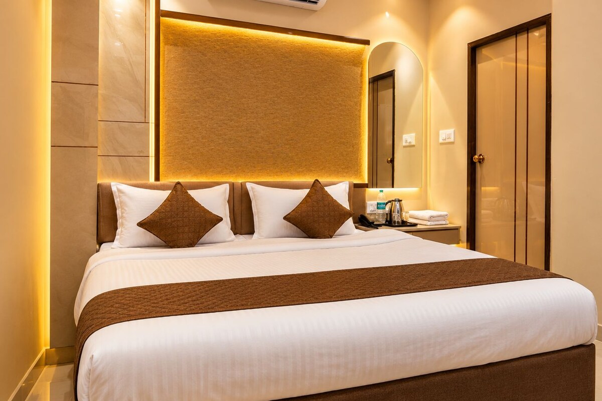 A hotel room with a large bed, a bedside table with a lamp, a mirror, and a wardrobe.
