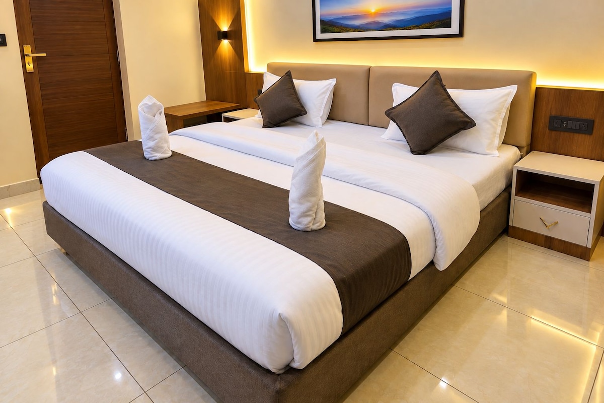 A hotel room with a large bed, two bedside tables, a nightstand, and a wall-mounted light.