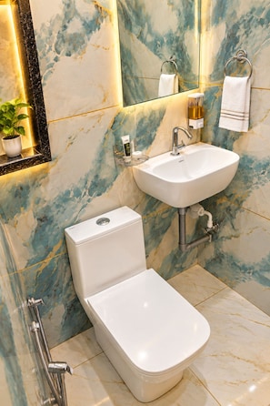 A modern bathroom with a toilet, sink, and a marble backsplash. - Hotel Ishaan Palace (Ujjain)