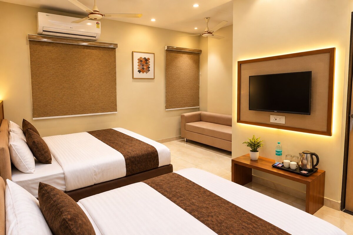 A hotel room with two beds, a sofa, a TV, and a small table with amenities.