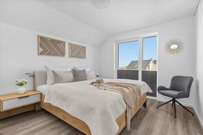 A bedroom with a bed, bedside tables, a chair, and a window with blinds. - Sonne und Mond - balcony, fireplace, infrared cabin, close to the beach, parking (Olpenitz)