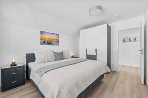 Um quarto moderno com cama, mesas de cabeceira, guarda-roupa e um quadro na parede.