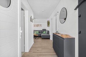 A modern interior with a hallway leading to a living area, featuring a grey sofa, a wooden sideboard, and decorative wall art. - Sonne und Mond - balcony, fireplace, infrared cabin, close to the beach, parking (Olpenitz)
