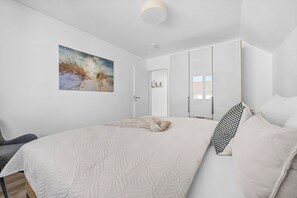 Une chambre à coucher avec un grand lit, un tableau représentant une scène de plage et une armoire avec un miroir.