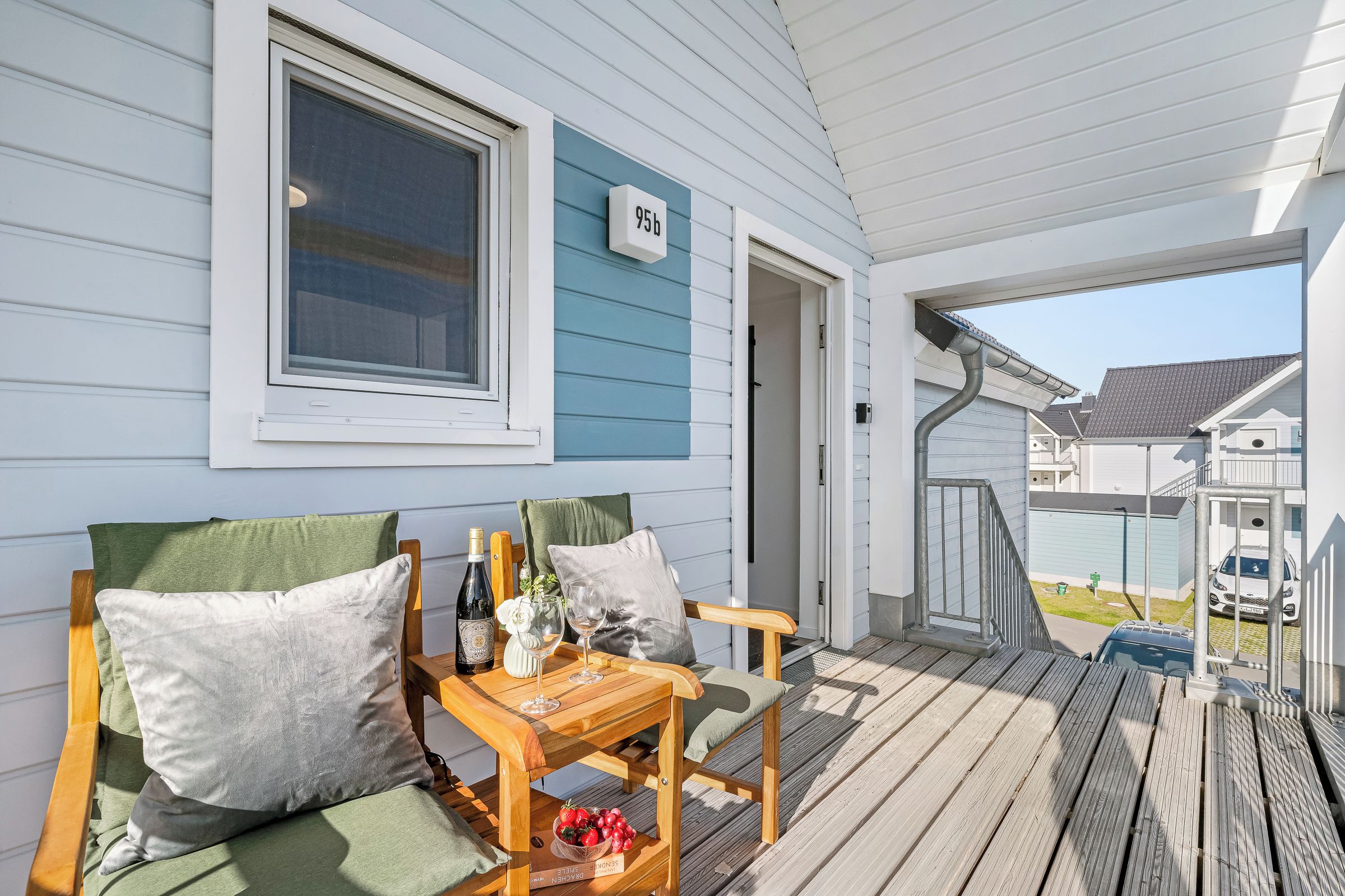 A wooden deck with a seating area, a bottle of wine, and a bowl of fruit.