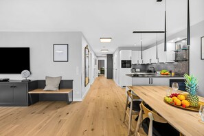 A modern kitchen with white cabinets, a wooden dining table, and a fruit bowl. - Westside Penthouse with a sauna, fireplace, balcony, and underground parking space (Sylt)