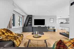 A modern living room with a sofa, a coffee table, a fireplace, and a TV. - Westside Penthouse with a sauna, fireplace, balcony, and underground parking space (Sylt)