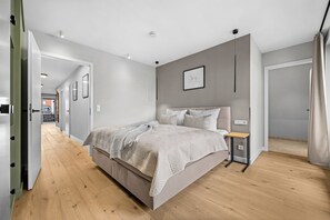 Un dormitorio moderno con una cama grande, una mesita de noche y una puerta que da a otra habitación.