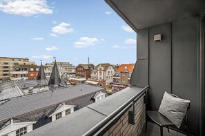 A balcony with a view of a cityscape, including buildings with varied architectural styles and a clear sky. - Westside Penthouse with a sauna, fireplace, balcony, and underground parking space (Sylt)