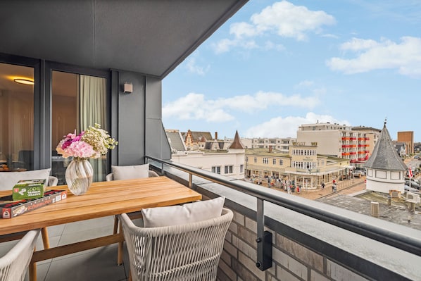 A balcony with a wooden table and wicker chairs, overlooking a cityscape with historic buildings and a church steeple. - Eastside Penthouse with a sauna, fireplace, balcony, and underground parking space (Sylt)