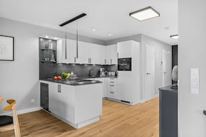 A modern kitchen with white cabinets, a black countertop, and a built-in oven. - Eastside Penthouse with a sauna, fireplace, balcony, and underground parking space (Sylt)
