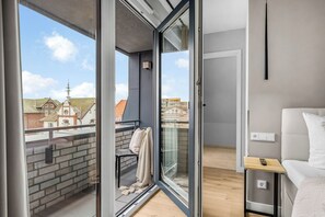 A modern apartment with a balcony, a bed, and a view of a church and buildings. - Eastside Penthouse with a sauna, fireplace, balcony, and underground parking space (Sylt)