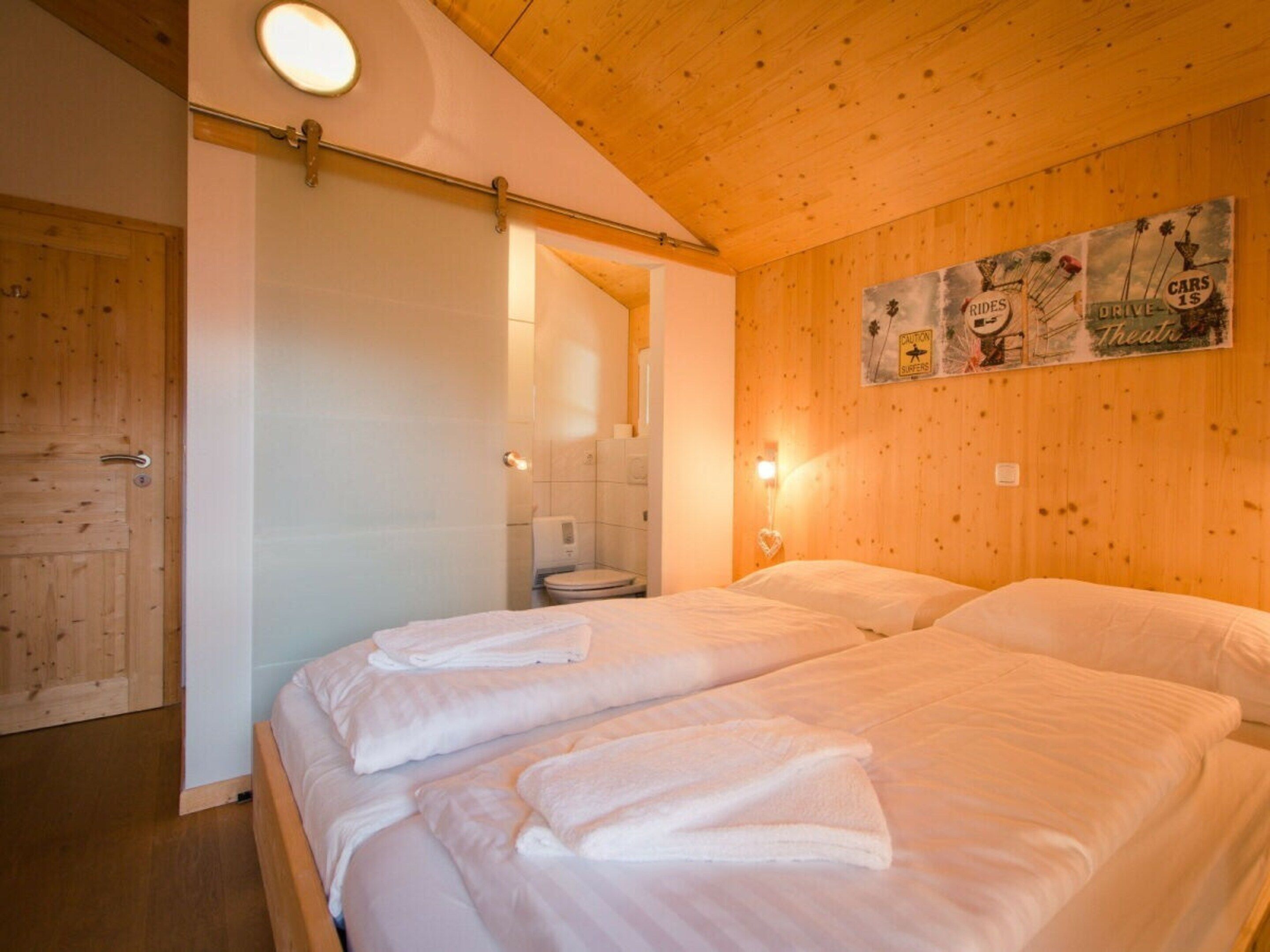 A hotel room with two beds, a wooden ceiling, a wall-mounted light, and a poster advertising rides and theater.