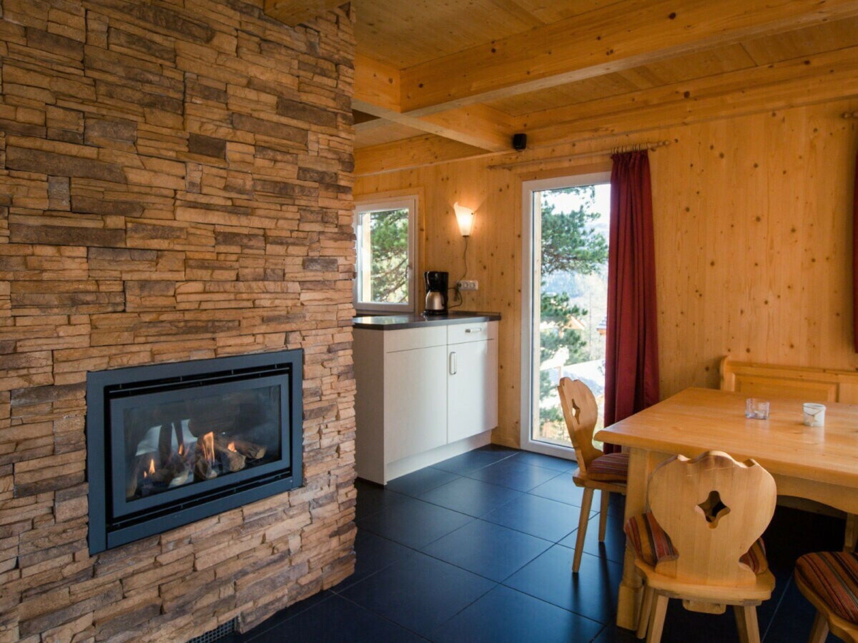 A cozy room with a stone fireplace, wooden ceiling, and a dining area with chairs and a table.