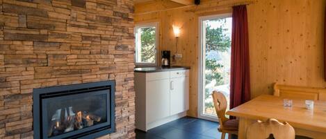 A cozy room with a stone fireplace, wooden ceiling, and a dining area with chairs and a table.