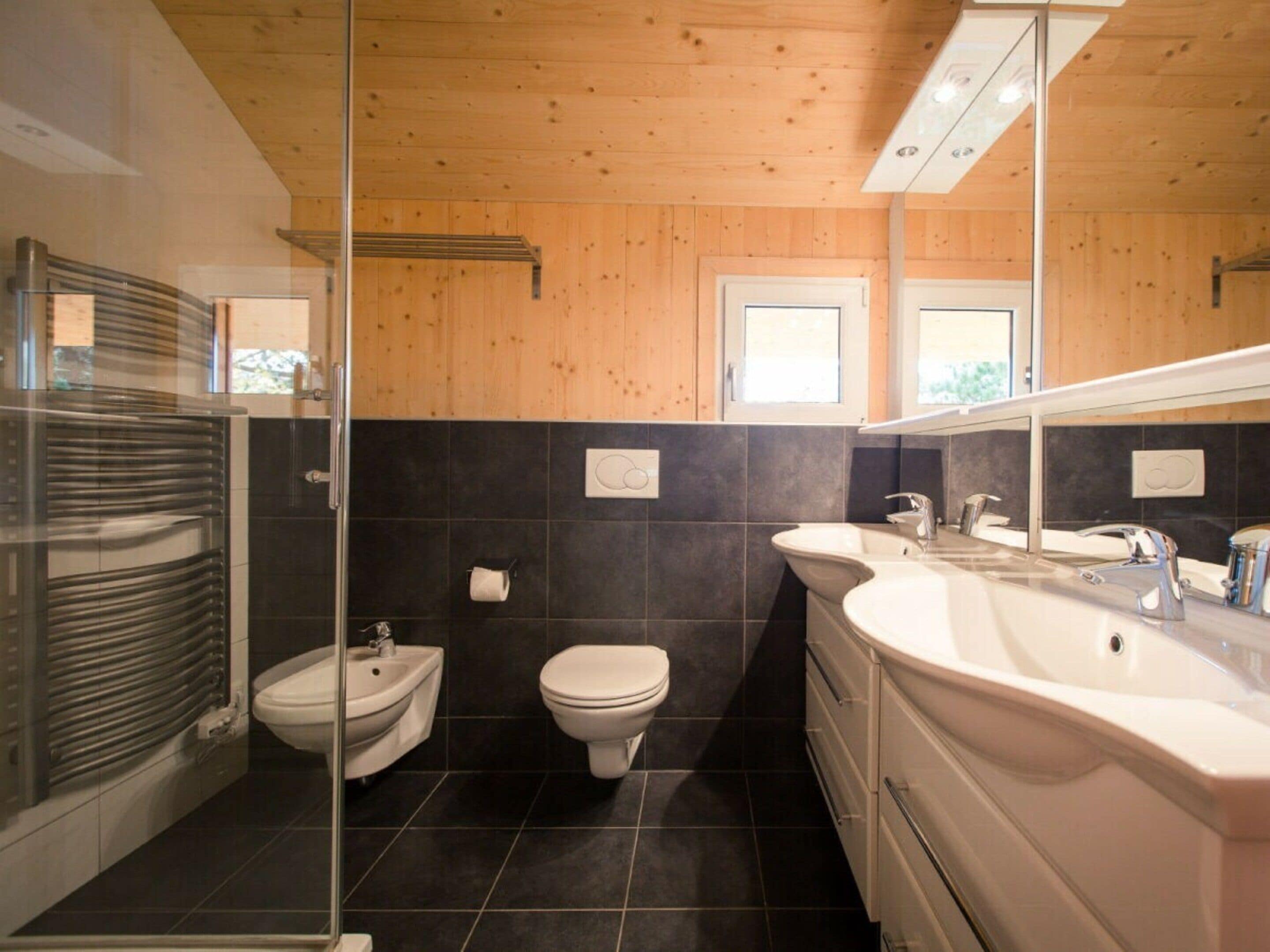 Une salle de bain moderne dotée d’une douche à parois de verre, d’un bidet, de toilettes et d’un meuble-lavabo avec un grand miroir.
