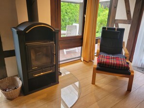 A room with a fireplace, a chair with a plaid cushion, and a view of greenery outside. - Experience pure relaxation at the family-friendly KÜSTENKIND vacation home in Burhav (Burhave)