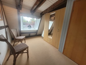 A room with a sloped ceiling, a large window, a wardrobe, and two wicker chairs. - Experience pure relaxation at the family-friendly KÜSTENKIND vacation home in Burhav (Burhave)