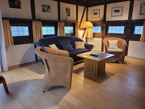 A room with a blue sofa, a wicker chair, a wooden coffee table, and a lamp. - Experience pure relaxation at the family-friendly KÜSTENKIND vacation home in Burhav (Burhave)