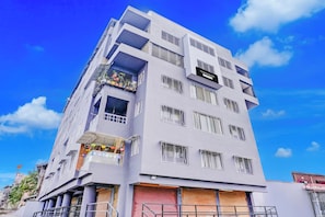 Um edifício de vários andares com sacadas, uma placa indicando que é uma casa geminada, e um céu azul claro ao fundo.